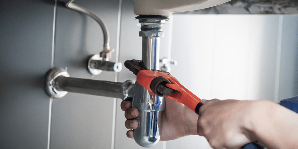 Plumber tightens sink trap after fixing a clogged pipe.