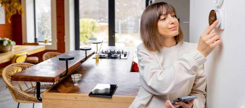 HVAC Services Female homeowner adjusts settings on her smart thermostat.