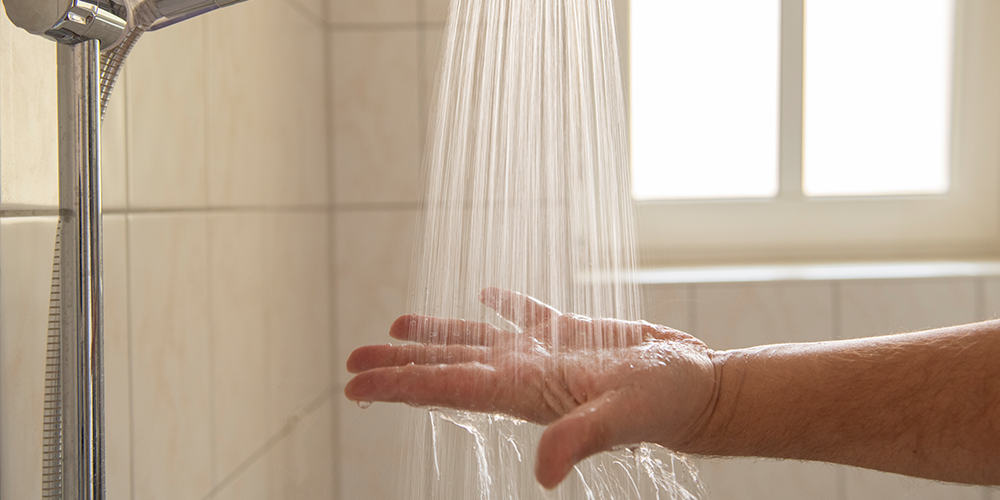 Male homeowner stick arm under shower stream to test for water heater problems.